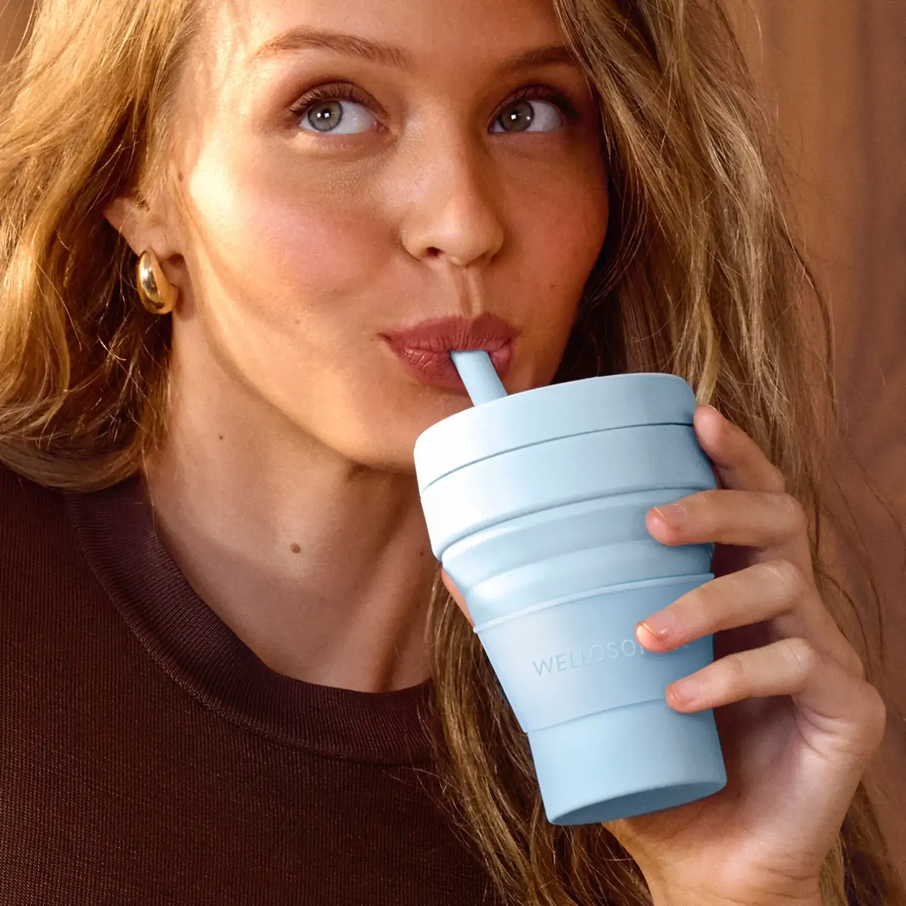 Mujer tomando de un vaso plegable con popote