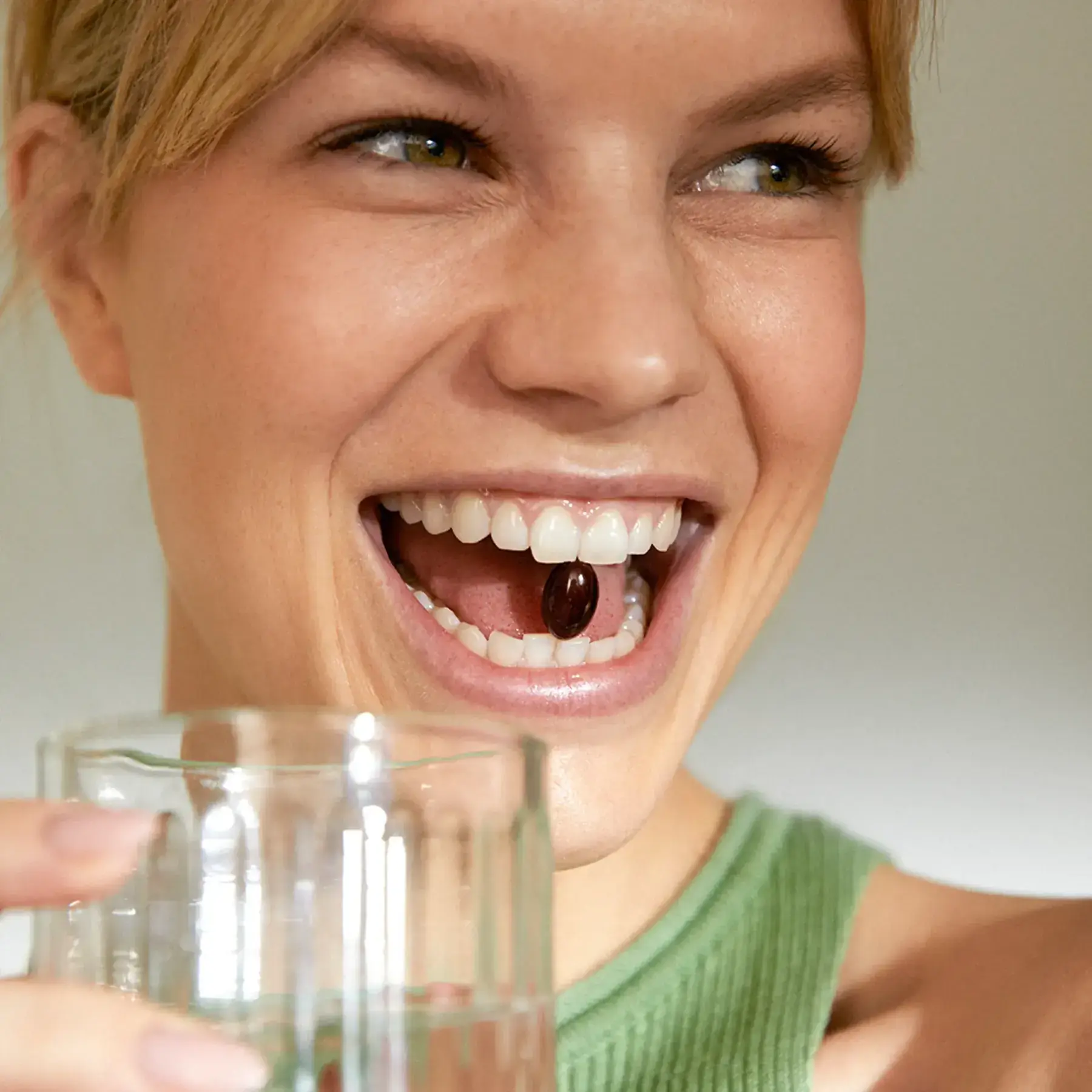 Mujer riendo con una cápsula de astaxantina entre los dientes